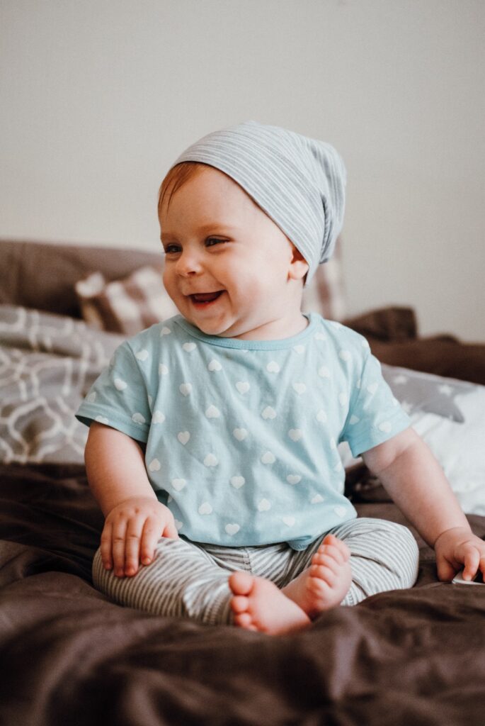 Cute little happy baby girl plays sitting on a bed in a room. Happy family having fun.